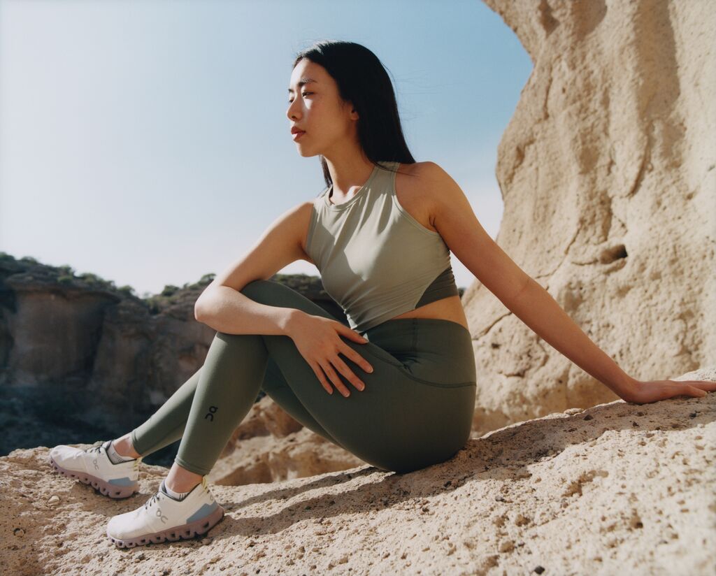 Young woman in workout gear and On Running Shoes sitting, looking wistfully off camera